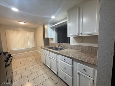 Kitchen with black range with gas cooktop, white cabinetry, light tile patterned floors, and recessed lighting