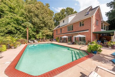 Gunite Pool with bathhouse to the left and covered patio to the right accessible via sidewalk to the circle driveway