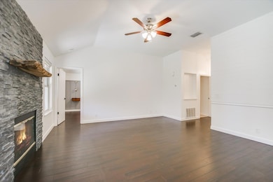 Unfurnished living room with lofted ceiling, dark wood-style floors, a stone fireplace, and ceiling fan