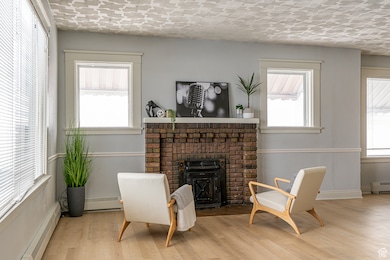 Sitting room featuring a textured ceiling, a brick fireplace, wood finished floors, and a baseboard radiator