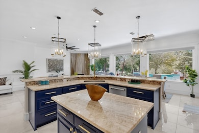 Kitchen featuring blue cabinetry, hanging light fixtures, light stone counters, open floor plan, and ornamental molding