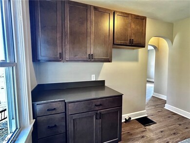Kitchen with arched walkways, dark countertops, dark wood-style flooring, and dark brown cabinets