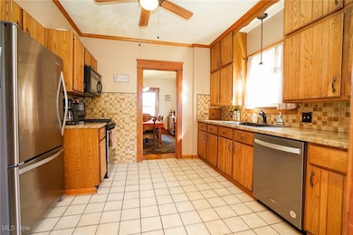 Kitchen with stainless steel appliances, brown cabinets, light countertops, backsplash, and ornamental molding