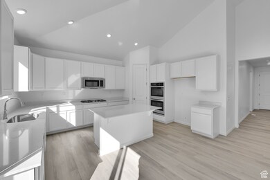 Kitchen with a breakfast bar, a center island, light wood-style flooring, white cabinetry, and high vaulted ceiling