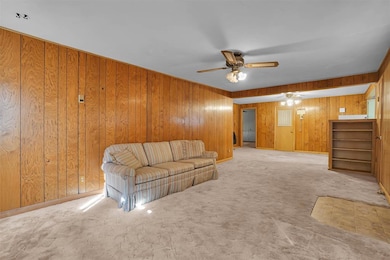 Unfurnished living room featuring wooden walls, carpet floors, and a ceiling fan