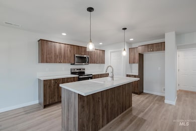 Kitchen with stainless steel appliances, light countertops, decorative light fixtures, light wood-style flooring, and recessed lighting