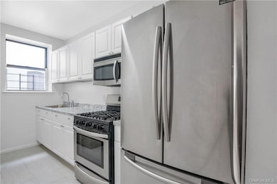 Kitchen with light stone counters, stainless steel appliances, sink, and white cabinets