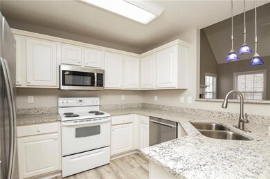 Kitchen featuring stainless steel appliances, a sink, light wood-style floors, white cabinetry, and vaulted ceiling