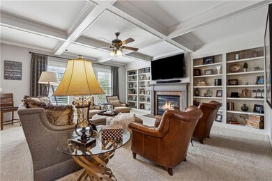 Carpeted living area with a fireplace with flush hearth, crown molding, beamed ceiling, ceiling fan, and coffered ceiling