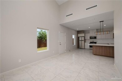 Kitchen featuring modern cabinets, light marble finish floors, stainless steel appliances, brown cabinetry, and a high ceiling