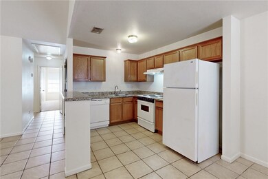 Kitchen with white appliances, light tile patterned flooring, brown cabinets, and under cabinet range hood