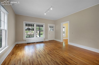 Spare room featuring radiator, rail lighting, wood finished floors, crown molding, and baseboards