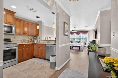 Kitchen with brown cabinetry, appliances with stainless steel finishes, light stone counters, crown molding, and tasteful backsplash