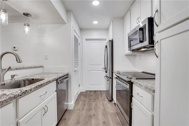 Kitchen featuring appliances with stainless steel finishes, a sink, white cabinets, light wood-style flooring, and recessed lighting
