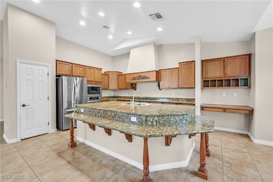 Kitchen with brown cabinets, a kitchen breakfast bar, light stone counters, appliances with stainless steel finishes, and light tile patterned floors