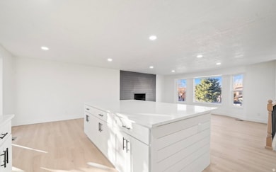 Kitchen with white cabinets, light wood finished floors, a center island, recessed lighting, and open floor plan