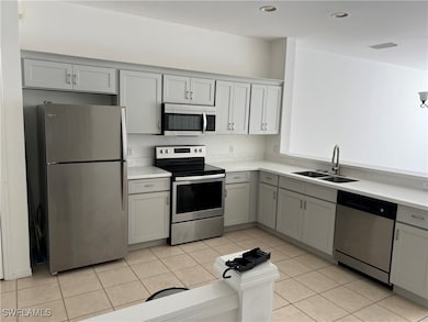 Kitchen featuring appliances with stainless steel finishes, light tile patterned floors, gray cabinetry, and sink