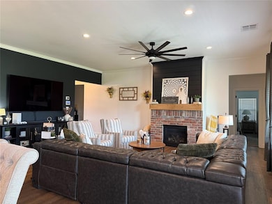 Living room featuring wood finished floors, ceiling fan, a brick fireplace, ornamental molding, and recessed lighting