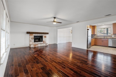 Unfurnished living room featuring light wood-type flooring, ceiling fan, crown molding, and a stone fireplace