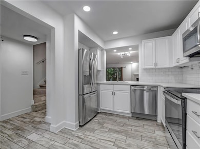 Kitchen featuring white cabinets, stainless steel appliances, wood finish floors, tasteful backsplash, and recessed lighting