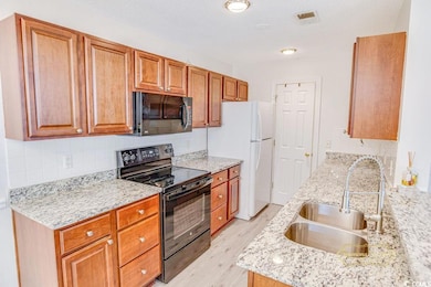 Kitchen with black appliances, tasteful backsplash, light wood-type flooring, brown cabinetry, and light stone countertops