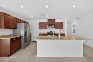 Kitchen with stainless steel appliances, recessed lighting, light stone countertops, an island with sink, and light tile patterned floors