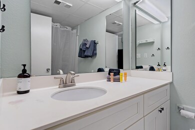 Bathroom with a textured wall, vanity, visible ven