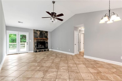 Unfurnished living room featuring a ceiling fan, a stone fireplace, vaulted ceiling, a chandelier, and light tile patterned floors
