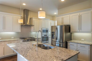 Kitchen with appliances with stainless steel finishes, wall chimney exhaust hood, decorative light fixtures, and a center island with sink