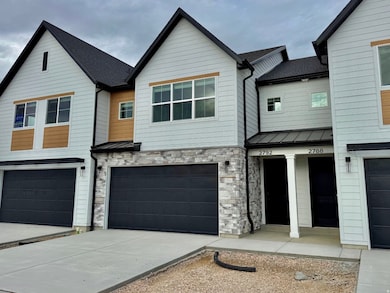 View of front of property featuring a standing seam roof, a metal roof, stone siding, an attached garage, and driveway