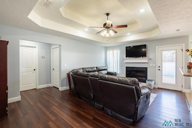 Living area featuring a glass covered fireplace, a raised ceiling, dark wood finished floors, ceiling fan, and a textured ceiling