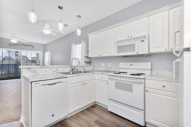 Kitchen with white appliances, a sink, a peninsula, white cabinetry, and light countertops