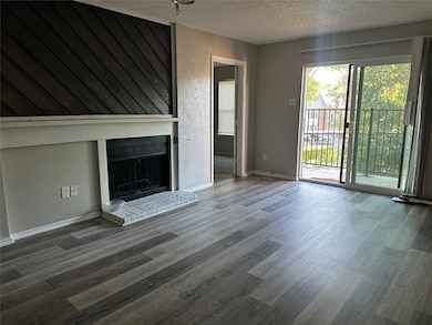 Unfurnished living room featuring a textured wall, a brick fireplace, a textured ceiling, and wood finished floors