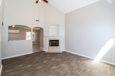 Unfurnished living room featuring high vaulted ceiling, wood finished floors, a fireplace, a ceiling fan, and arched walkways