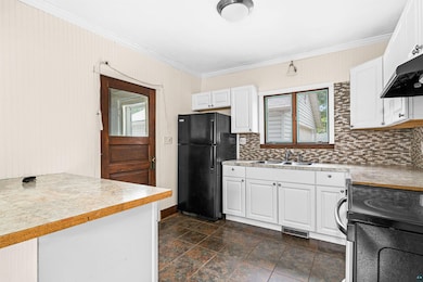 Kitchen featuring freestanding refrigerator, crown molding, decorative backsplash, and healthy amount of natural light