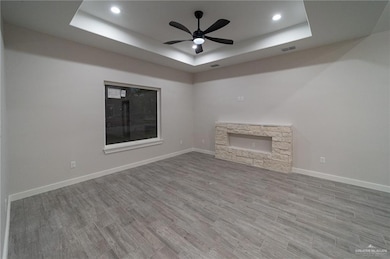 Unfurnished living room featuring a fireplace, a raised ceiling, wood finished floors, ceiling fan, and recessed lighting