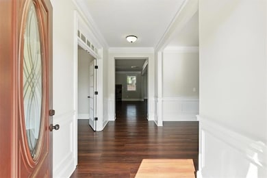 Foyer with wainscoting, dark wood-style floors, a decorative wall, and crown molding