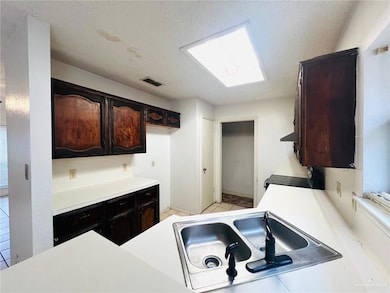 Kitchen featuring range, sink, a skylight, a textured ceiling, and dark brown cabinetry