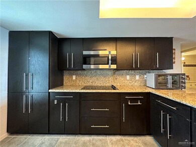 Kitchen featuring light stone countertops, light tile flooring, cooktop, and tasteful backsplash
