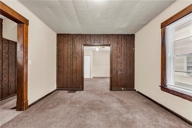 Empty room with a textured ceiling, carpet flooring, and wood walls