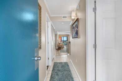 Hallway with light tile patterned flooring, visible vents, baseboards, and ornamental molding