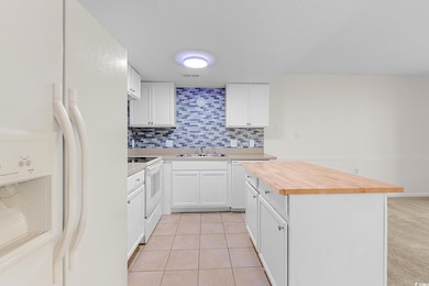 Kitchen with white appliances, wooden counters, decorative backsplash, a center island, and white cabinetry