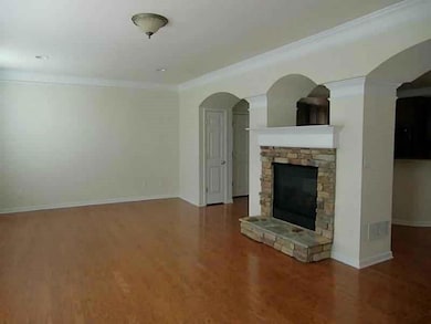 Unfurnished living room with a stone fireplace, arched walkways, dark wood finished floors, and ornamental molding