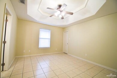 Empty room with a tray ceiling, ceiling fan, and light tile patterned flooring