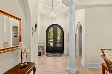 Entrance foyer with light tile patterned floors, arched walkways, french doors, a high ceiling, and a chandelier