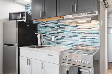 Kitchen with stainless steel appliances, under cabinet range hood, a sink, tasteful backsplash, and light stone counters