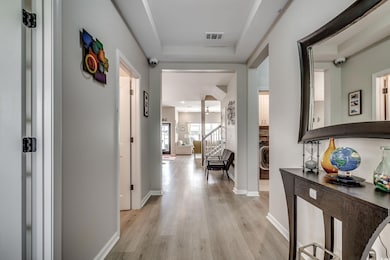Hall with light wood-style flooring, washer / clothes dryer, baseboards, and a raised ceiling