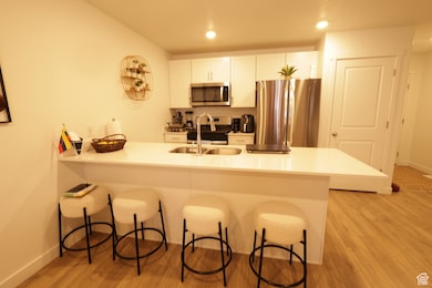 Kitchen featuring stainless steel appliances, a kitchen bar, white cabinets, a peninsula, and light wood-style floors