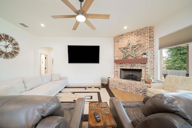 Living room with recessed lighting, a brick fireplace, wood finished floors, arched walkways, and a ceiling fan