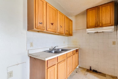 Kitchen featuring light countertops, a textured ceiling, tile walls, and under cabinet range hood